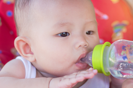 Portrait of cute baby on toy car drinking water of bottleの写真素材