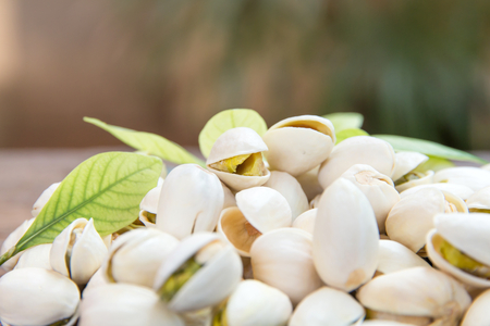Close up of Pistachios nuts on wooden table. Pistachio in wooden bowl in background with green leavesの写真素材