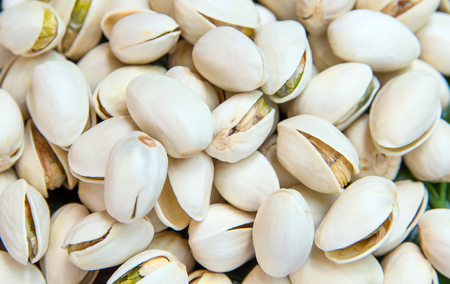 Close up of Pistachios nuts on wooden table. Pistachio in wooden bowl in background with green leavesの写真素材