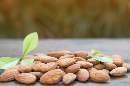 close up of almonds grain roast on wood background with green leavesの写真素材
