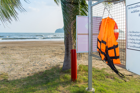 Orange life jackets hanging on a rack with warning label for first aid on beach background,Thai and English wordの写真素材