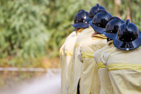 Firemen using water from hose for fire fighting at fire fight training of insurance group.Firefighter wearing a fire suit for safety under the danger training case.の写真素材