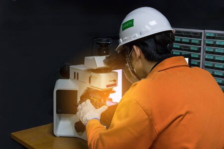 Asian man in orange suit with safety equipment used microscope check quality glass in QC lab dark roomの写真素材