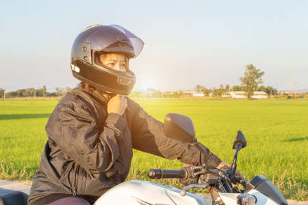 Asian woman with helmet and wearing and fasten before riding big bike motorcycle on the road for...