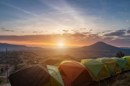 Many camping tent on green field near forest during dramatic sunrise at summer misty morning,Concept of outdoor camping adventureの写真素材