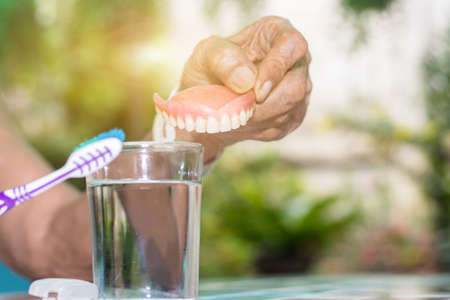 Old women hand hold fake teeth with dirty for removable partial denture cleaning with toothbrushの写真素材