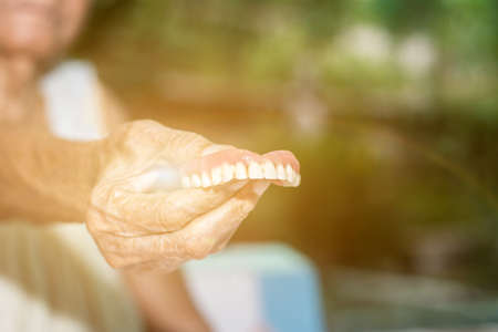 Old women hand hold fake teeth with dirty for removable partial denture cleaning with toothbrush