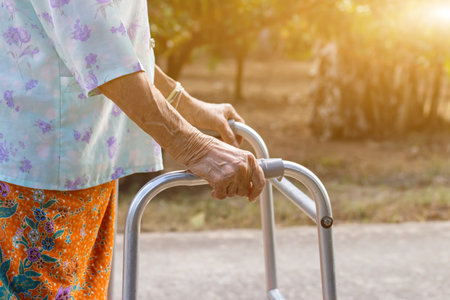 Asian old woman standing with her hands on a walker,Hand of old woman holding a staff cane for helping walkingの写真素材