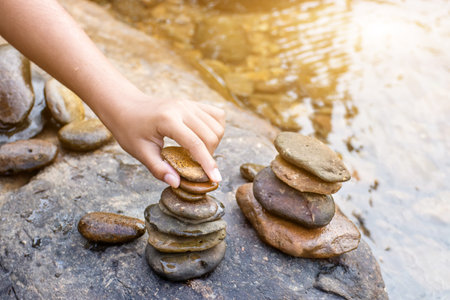 Child hand placing a rock stacks on top of a cairn on creek,Blurred background.の写真素材