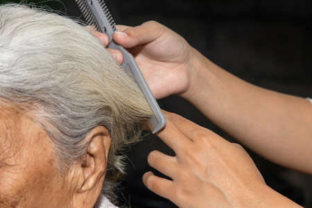 Hand of woman cutting her elderly mother's hair in nature at homeの写真素材