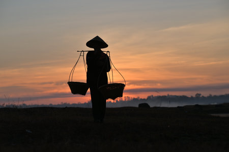 Thai farmers are carrying baskets to prepare to go home before the sun goes down. Silhouette farmer. Silhouette light.の写真素材
