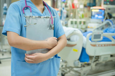 A nurse holds a patient history in hand and a stethoscope around her neck while visiting the patient with the doctor.の写真素材
