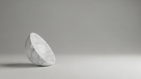 A cut marble bowl rests on a white surface, contrasting against a soft gray backdrop. The object has a natural texture with subtle color variations. The lighting is diffused, casting soft shadows. Suitable for use in design projects, presentations, or as a decorative element.の素材