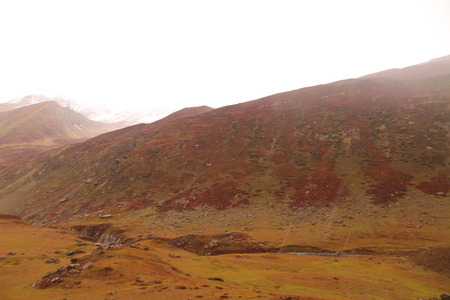 Mountains in autumn with brown and reddish grass under cloudy skyの写真素材
