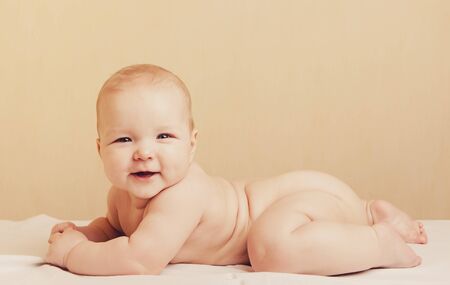 Cute baby lying on bedsheet and smiling at cameraの写真素材