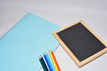 a piece of paper, black board and color pencils isolated on white backgroundの写真素材