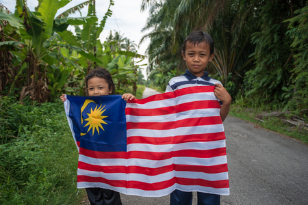 Portrait of playful and joyful two siblings of children with Malaysia flag in nature background, patriotic theme concept. Selective focus. Copy space.の写真素材