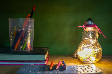 Creative layout of flat lay made of school accessories or student equipment includes books, pencil, alarm clock and ornaments on green and wood background. Selective focus. Educational, student life ideas concept.の写真素材