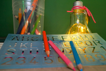 Creative layout of flat lay made of school accessories or student equipment includes books, pencil, alarm clock and ornaments on green and wood background. Selective focus. Educational, student life ideas concept.の写真素材