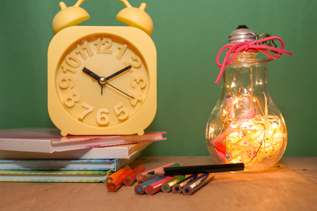 Creative layout of flat lay made of school accessories or student equipment includes books, pencil, alarm clock and ornaments on green and wood background. Selective focus. Educational, student life ideas concept.の写真素材
