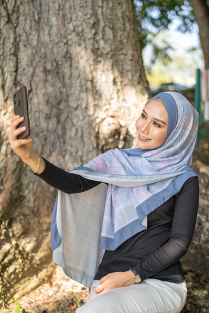 Happy young Asian woman take selfie with her smartphone at blurred park background.の写真素材