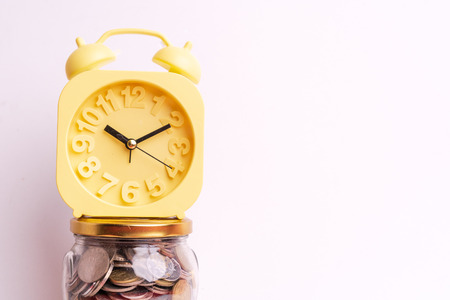 Coins in glass jar and yellow alarm clock isolated on white background. Future financial concept.