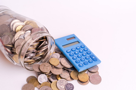 Coins in glass jar with blue mini calculator on white background isolated. Financial and economy...