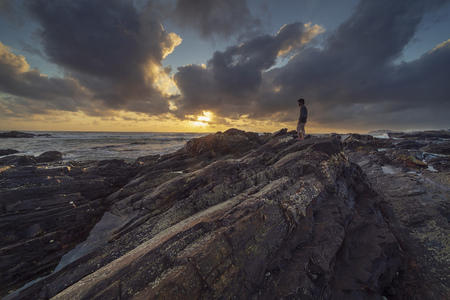 A man standing on rocks at beach side with stunning and dramatic clouds sunrise scenery at Pantai...