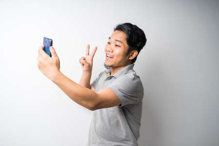 Portrait of young Asian man, taking self-portrait photograph or selfie isolated and selective focus.の写真素材