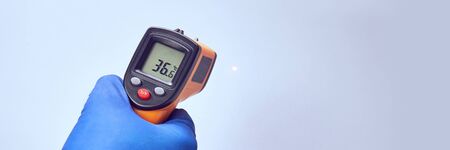 hand in blue glove holds ir thermometer high temperatureの写真素材