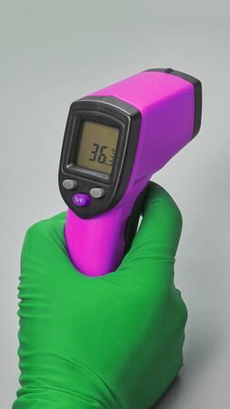 Hand in green glove holds thermometer normal temperatureの写真素材