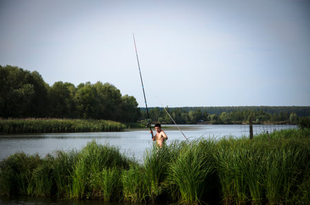 Fisherman with a fishing rod on a lake in the summerの写真素材