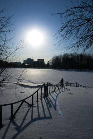 Winter landscape with frozen lake and fence in the city park at sunsetの写真素材