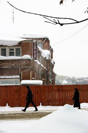 A man walking in a snow-covered street in front of a houseの写真素材
