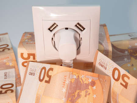An electrical socket with a connected plug and euro banknotes around it. Electricity cost and...