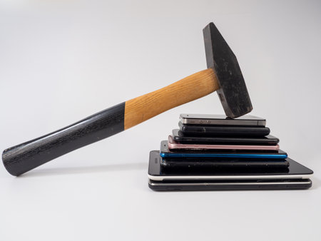 A hammer with a wooden handle breaks a stack of smartphones. Broken smartphones.