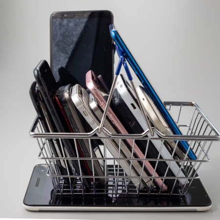 Phones of different models and generations are in the shopping cart. Smartphone on a gray...
