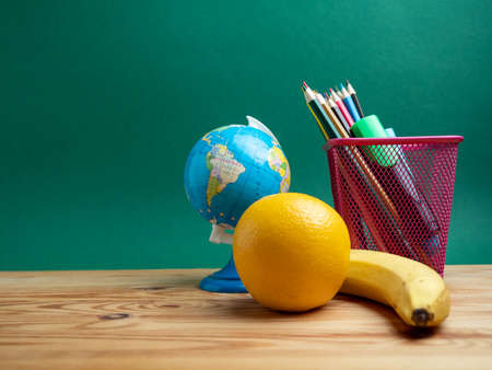 A book, a metal cup with pencils and a globe on the table against the background of a green board. School.の写真素材