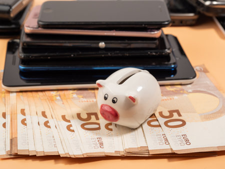 Lots of old smartphones, piggy bank and money on an orange background. Old mobile phones and euro banknotes. Broken smartphones.の写真素材