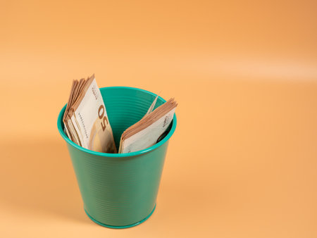 Money in the trash can on an orange background. Euros in the trash. Waste of money concept. Close up.の写真素材