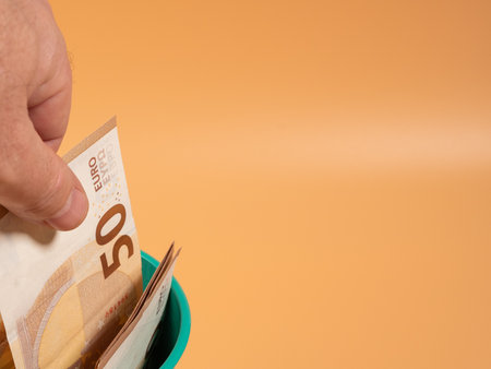Money in the trash can on an orange background. Euros in the trash. Waste of money concept. Close up.の写真素材