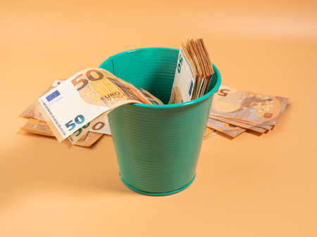 Money in the trash can on an orange background. Euros in the trash. Waste of money concept. Close up.の写真素材