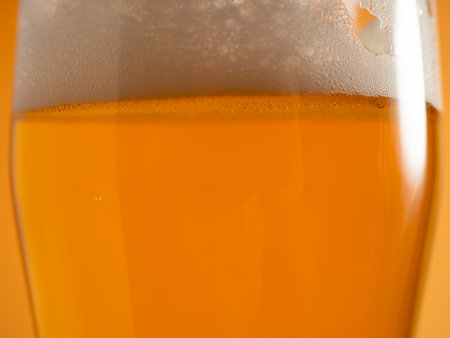 Glass of beer with foam. Mug of beer on an orange background. Close up.の写真素材