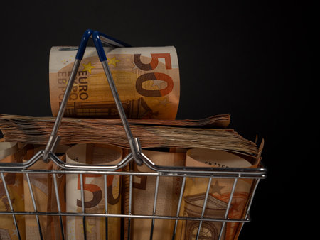 Shopping cart full of money. A shopping cart filled with euro banknotes. Shopping basket with money on a black background.の写真素材