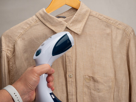 In hand Steamer for clothes. A shirt is ironed with a portable iron. Iron for ironing clothes.の写真素材
