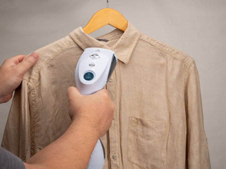 In hand Steamer for clothes. A shirt is ironed with a portable iron. Iron for ironing clothes.の写真素材