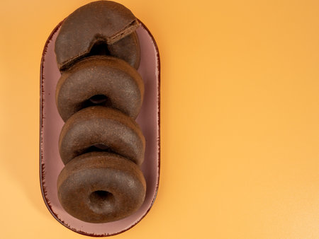 Fresh dark vegetarian donut on a plate on an orange background. Close up.の写真素材