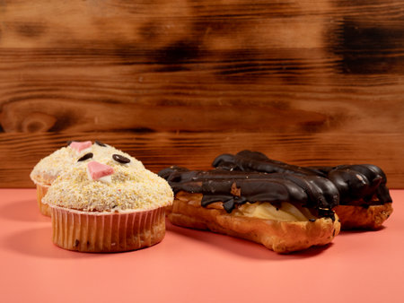 Muffin and chocolate eclairs isolated on pink background. Delicious sweets. Close up.の写真素材