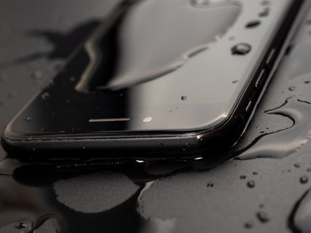 Water has been spilled on the smartphone. The smartphone fell into the water. Wet smartphone on a black background.の写真素材