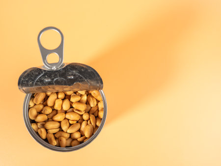 Roasted peanuts in an open jar on orange. Peanuts close up.